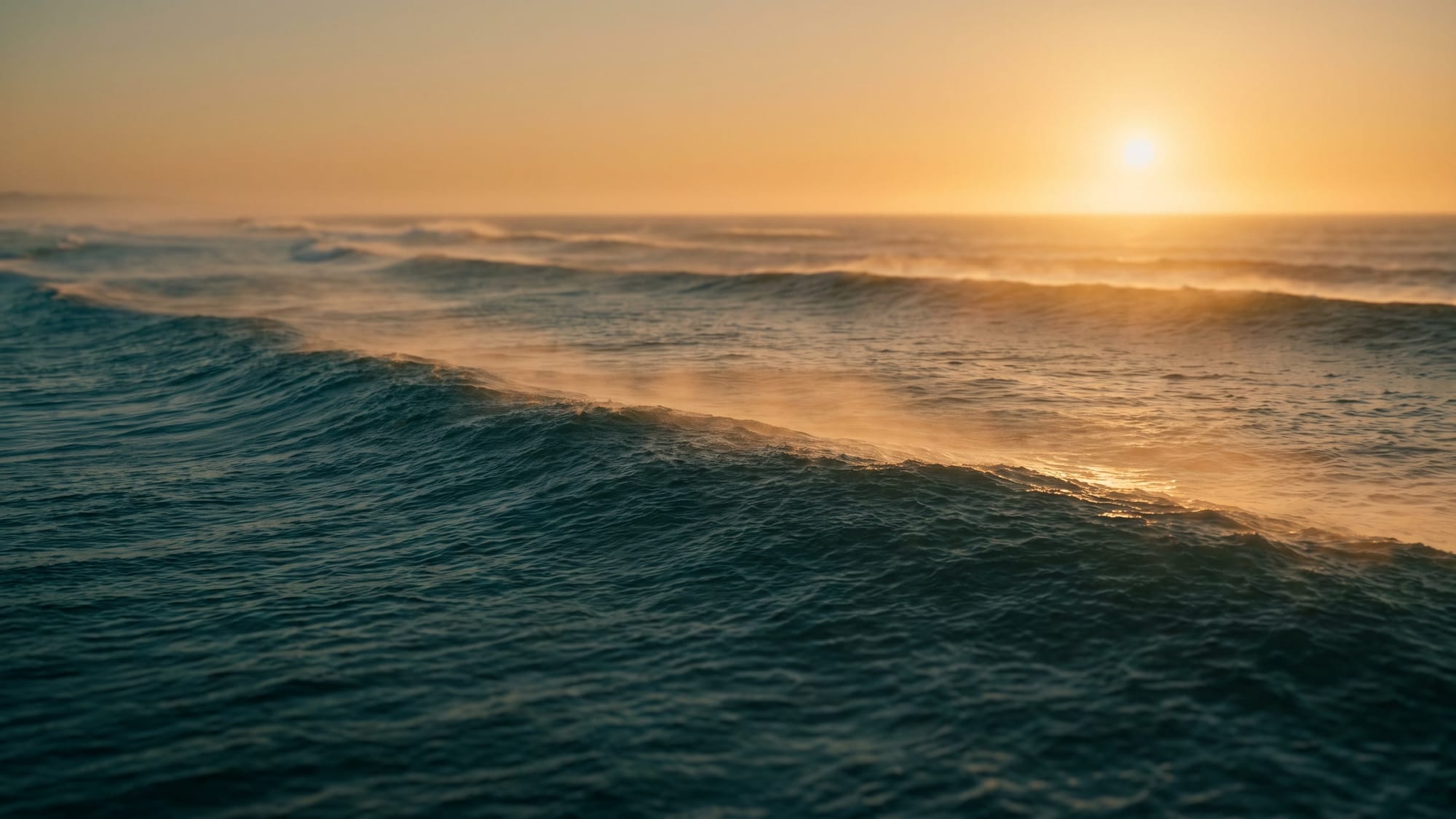 Long ocean swells under a low, hazy amber sun